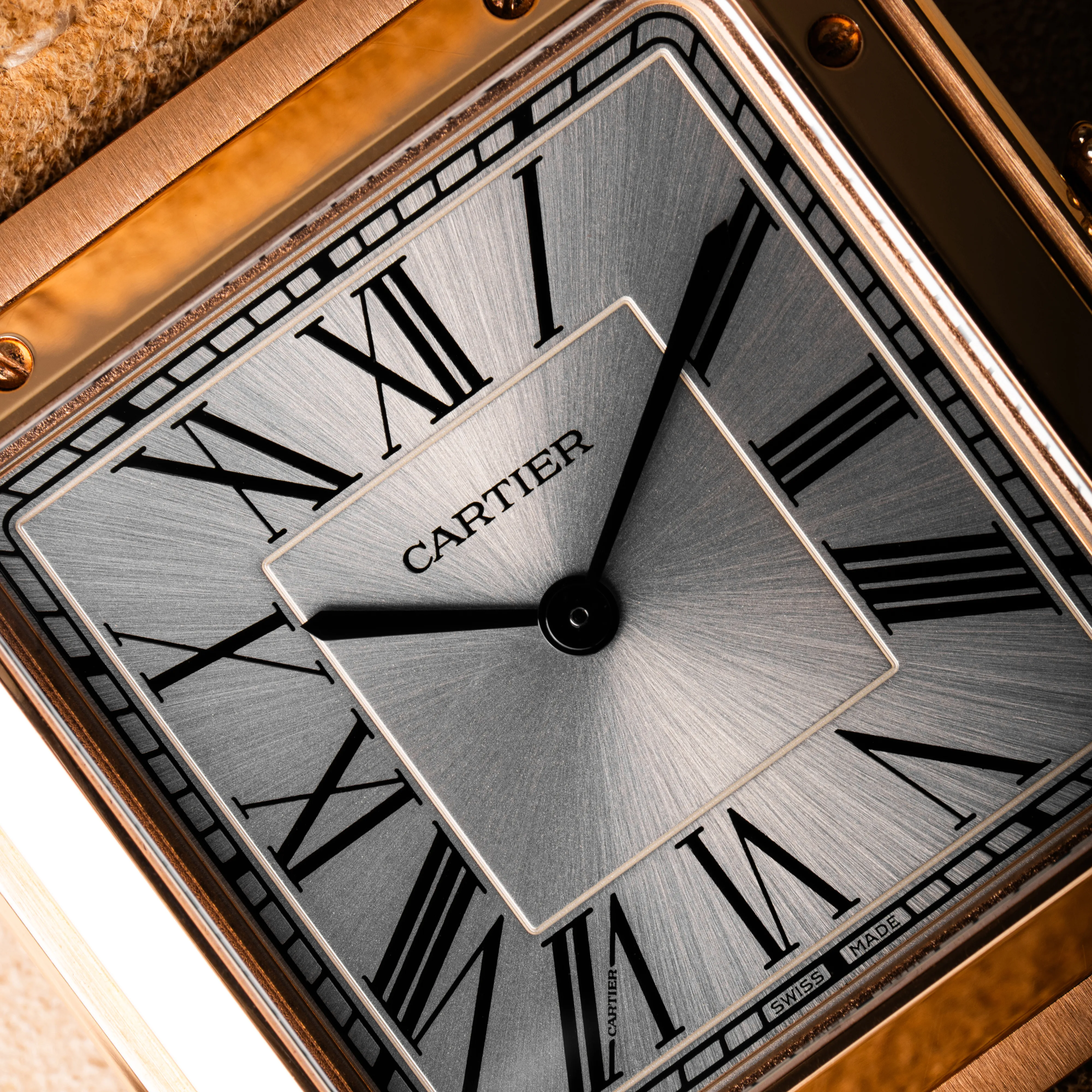Cartier Tank with rose gold case and beige leather strap resting on a red Cartier box with gold details